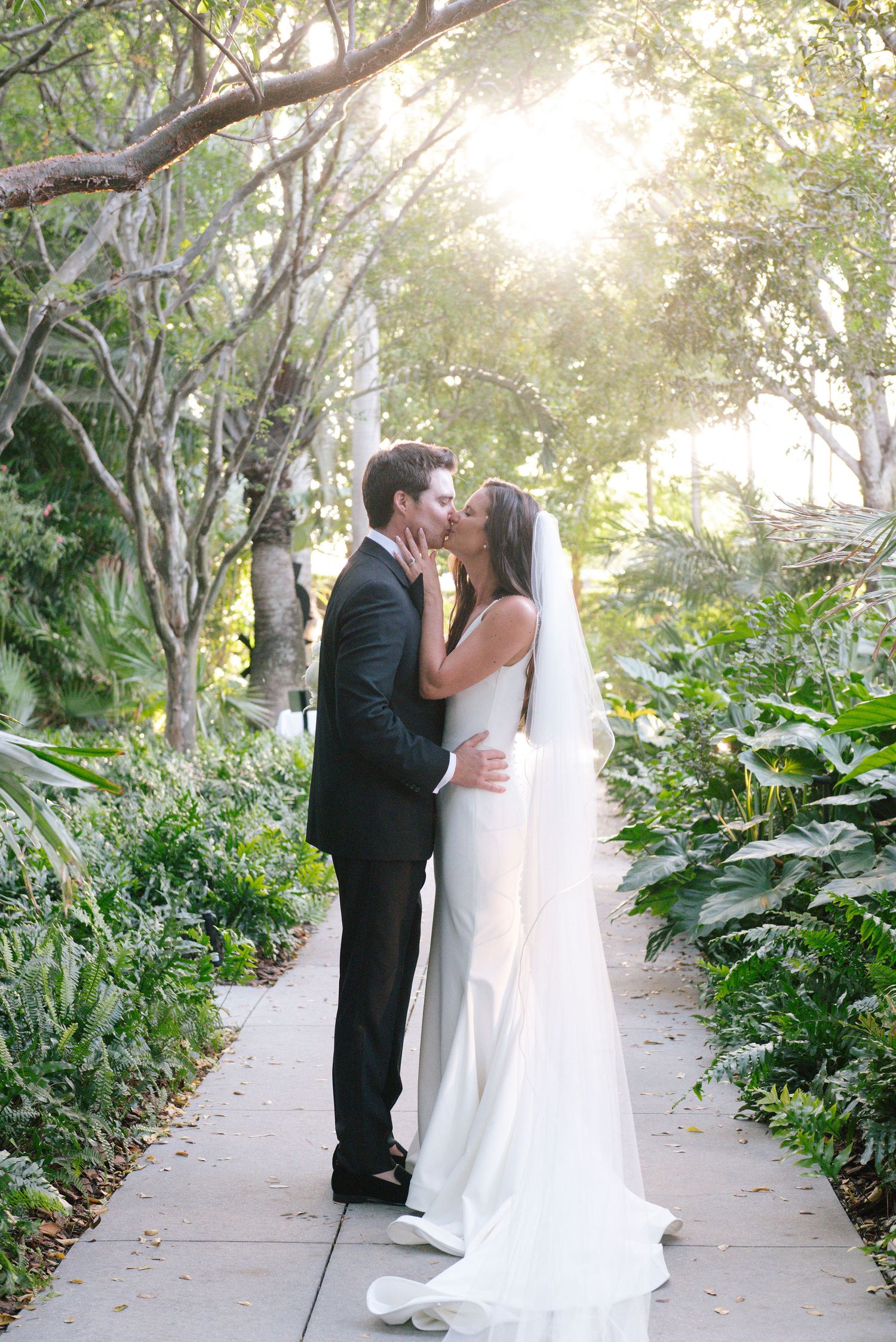 A couple shares an intimate moment on a sunlit garden path during their wedding day.