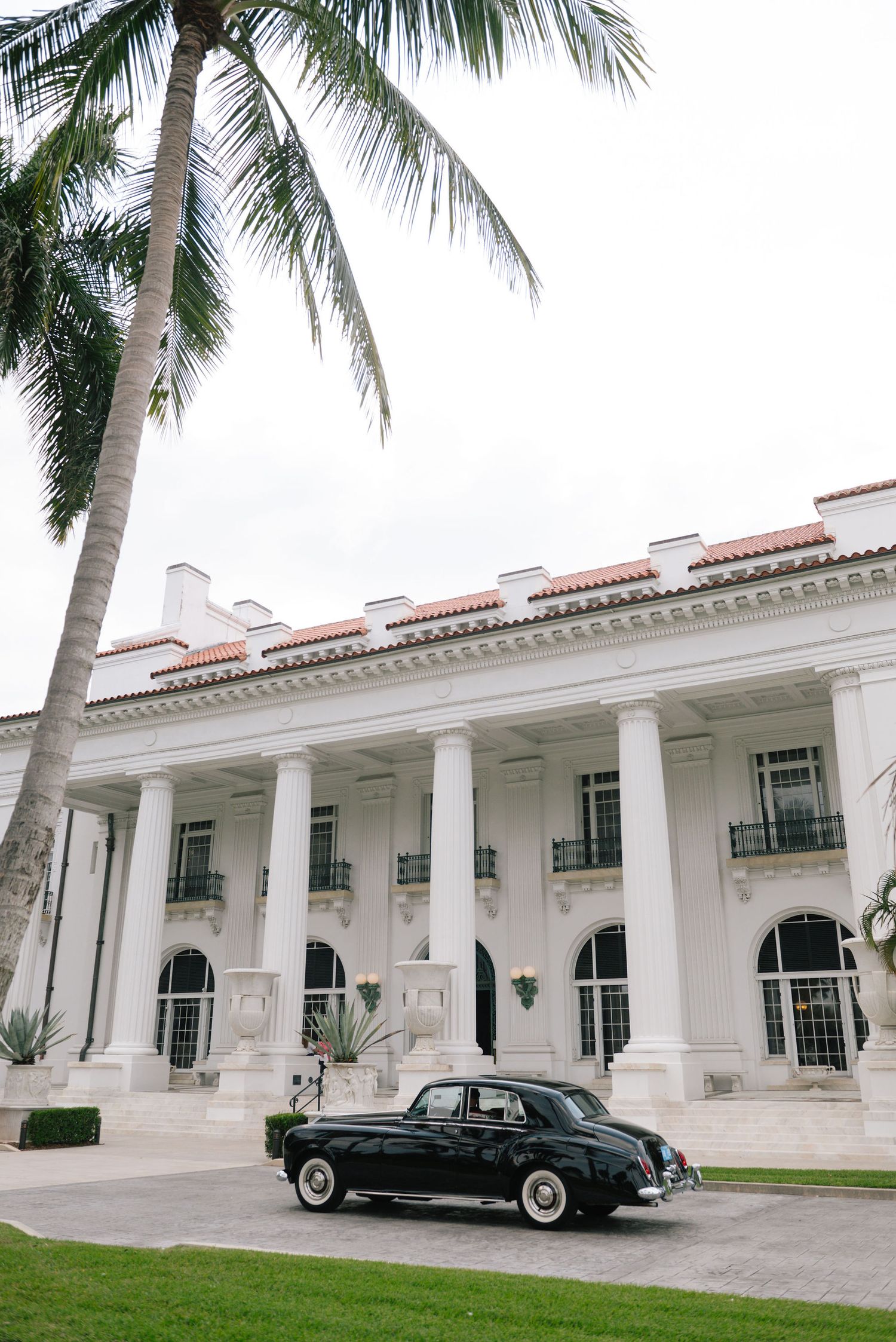 Elegant white colonial building with palm trees and vintage car in front.