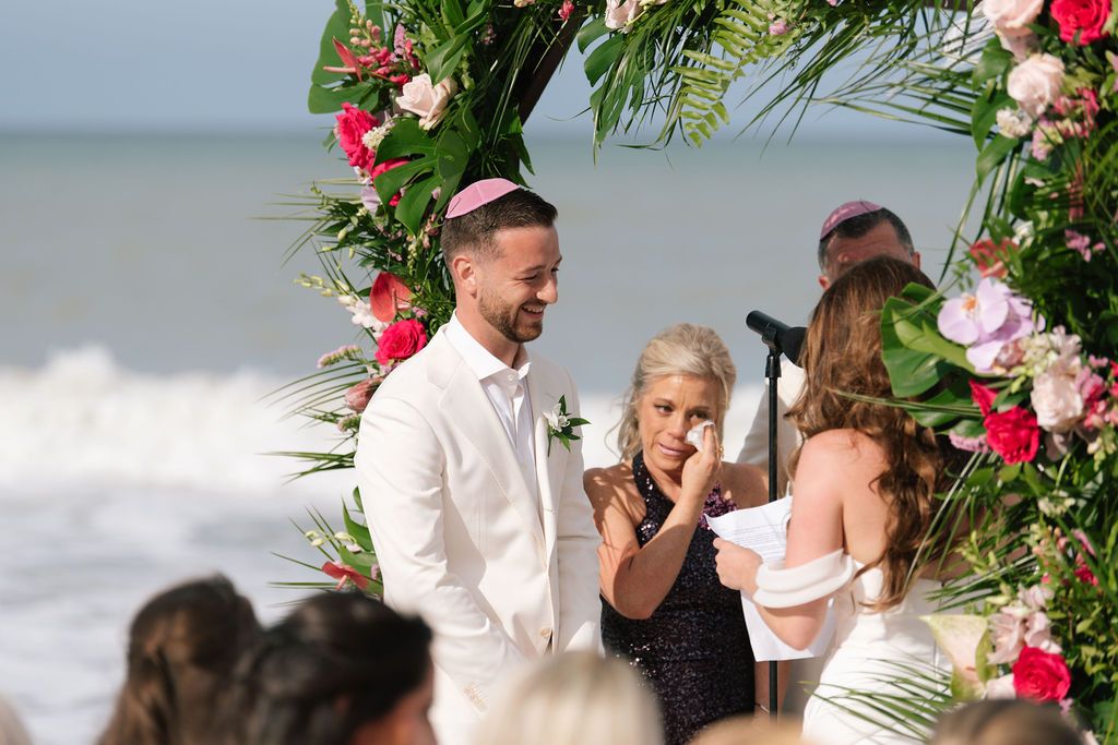 Wedding ceremony under floral arch with pink and white flowers by the ocean.