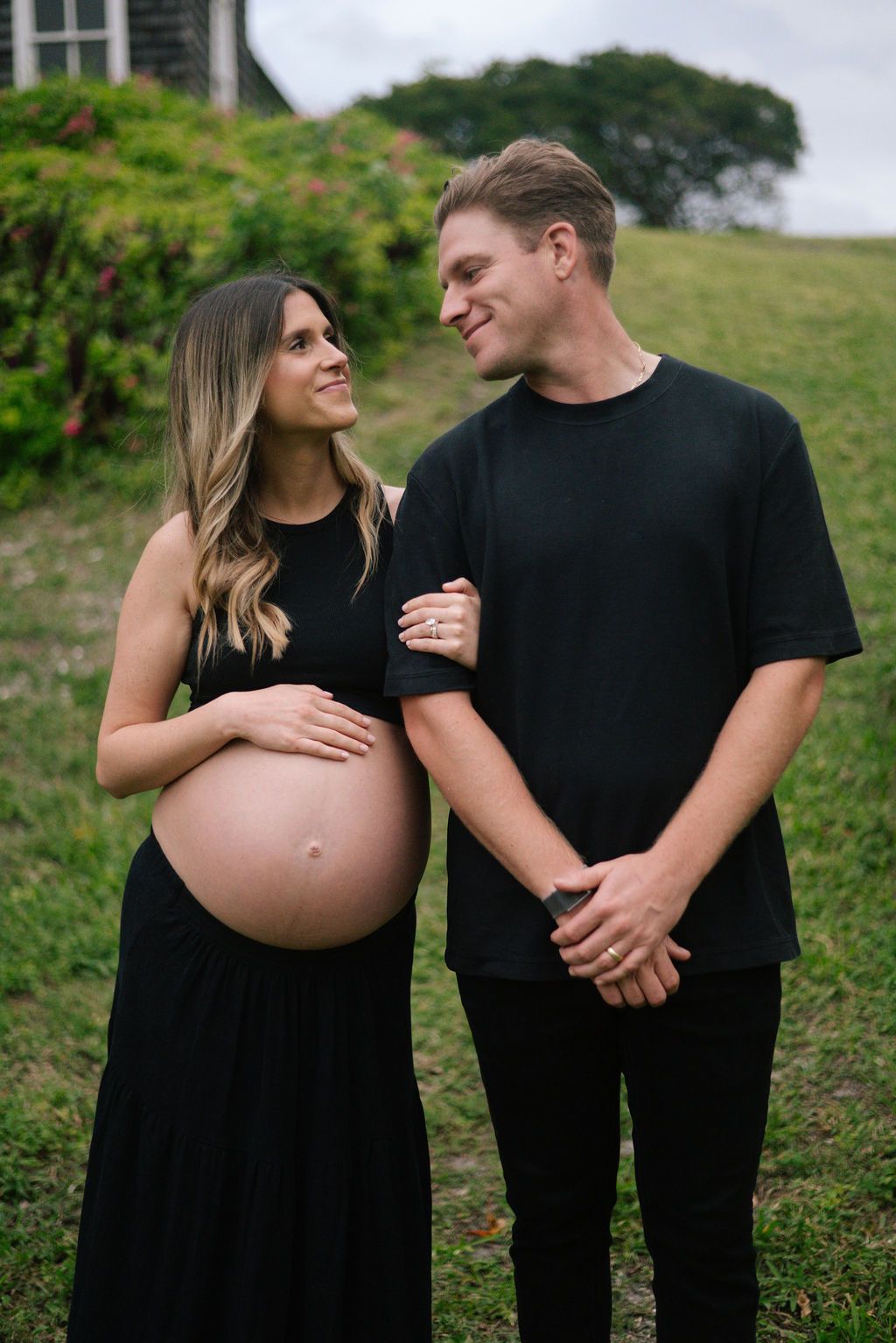 Expecting couple shares intimate moments while wearing matching black outfits outdoors.