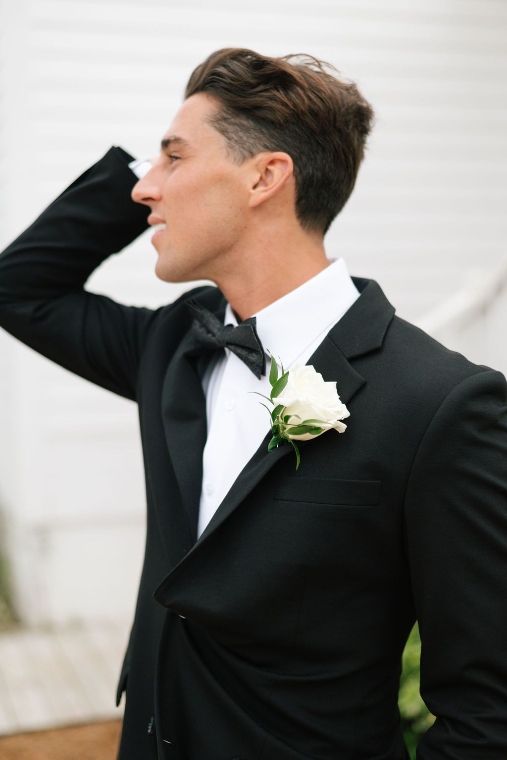Groom in classic tuxedo with white boutonniere poses against white background.