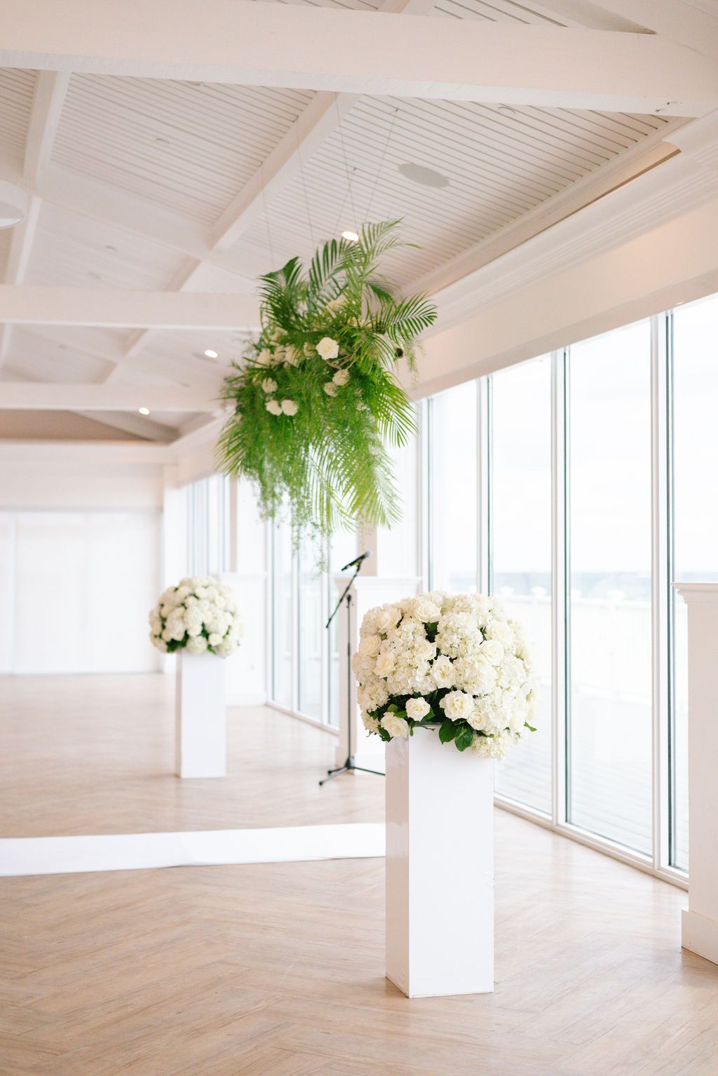 Airy white event space decorated with hanging floral arrangements and ferns.