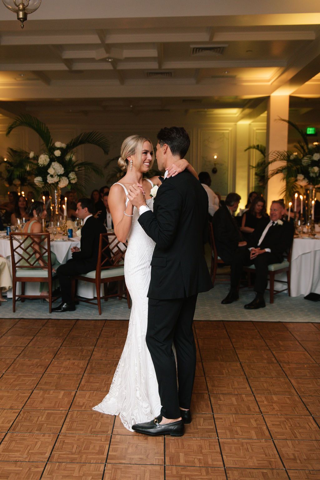 Romantic slow dance moment at an elegant wedding reception with palm decor and candlelit tables.