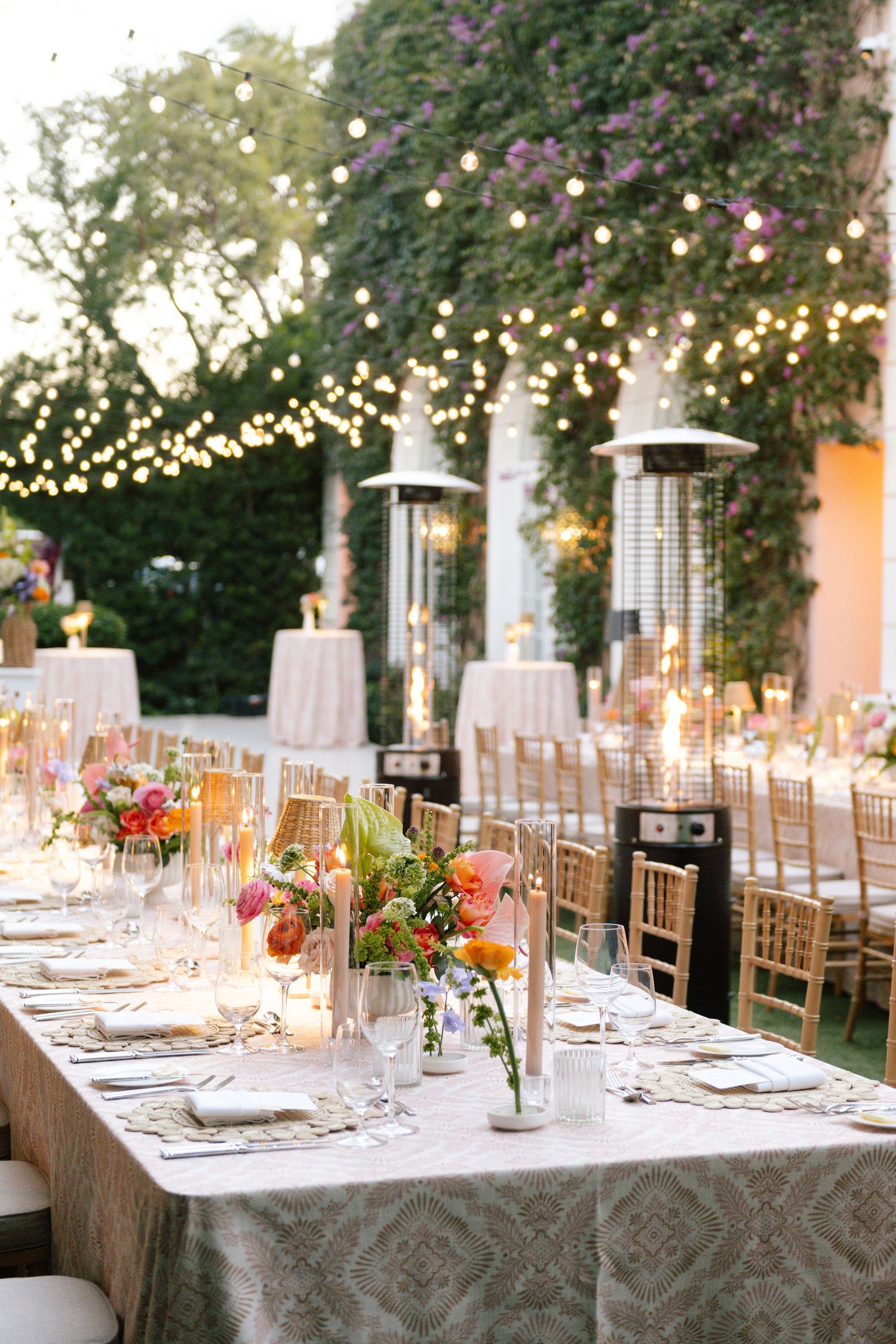 Wedding reception tables set with white linens and floral centerpieces under twinkling lights.