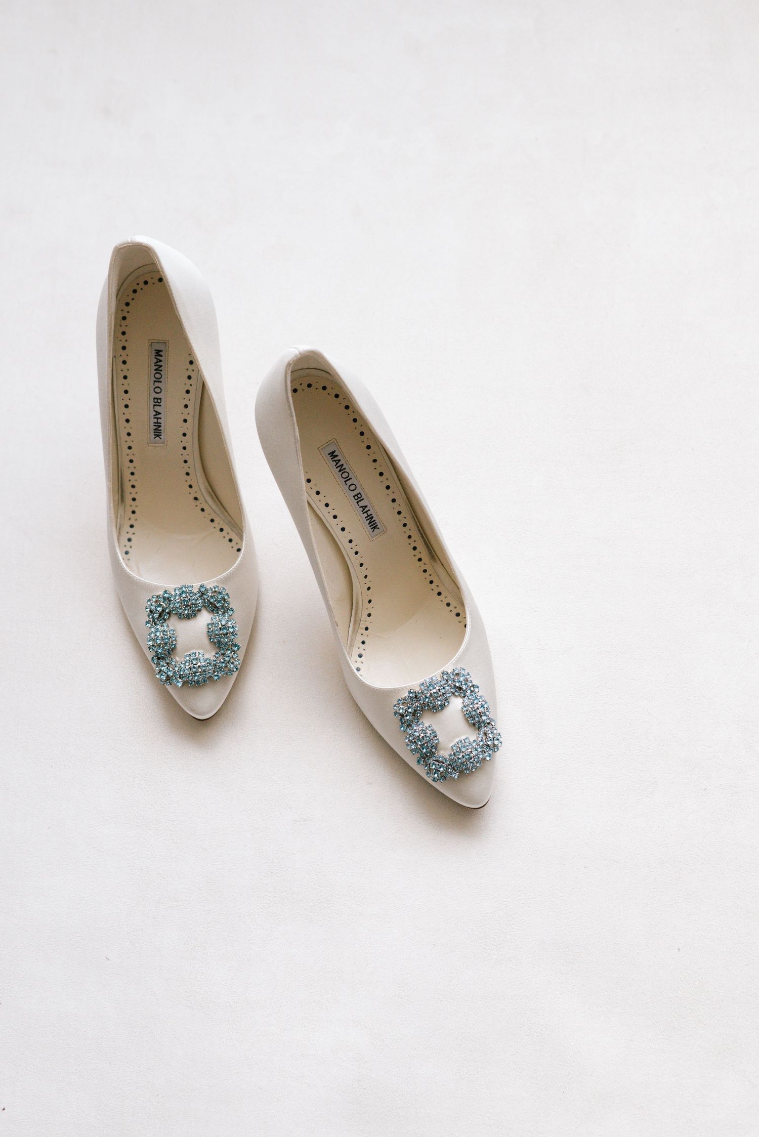 White Manolo Blahnik Hangisi heels with blue crystal buckles on white background.