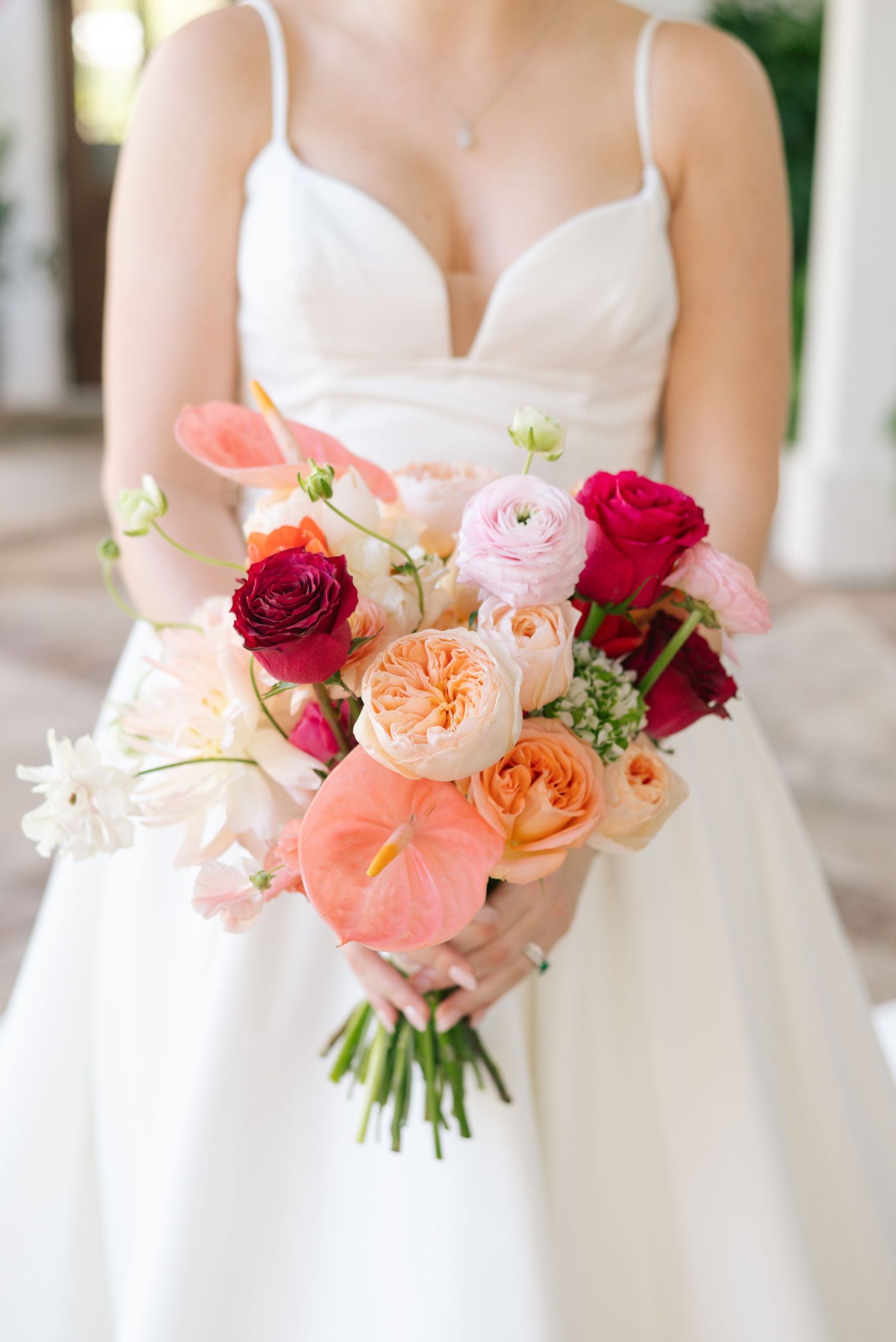 Coral and pink wedding bouquets with roses and peonies against white dresses.