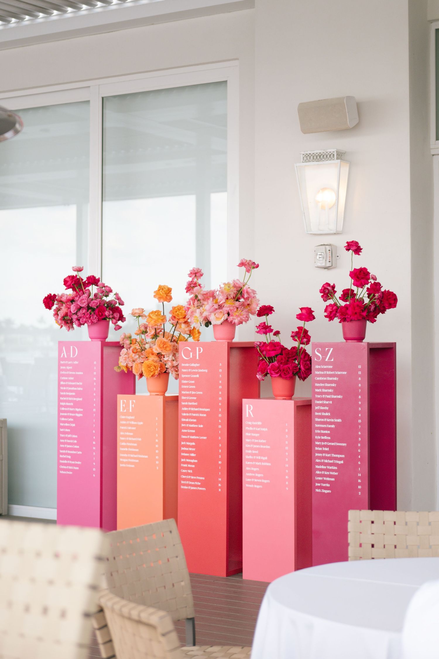 Pink and coral seating chart displays with fresh flowers in matching vases arranged on pedestals.