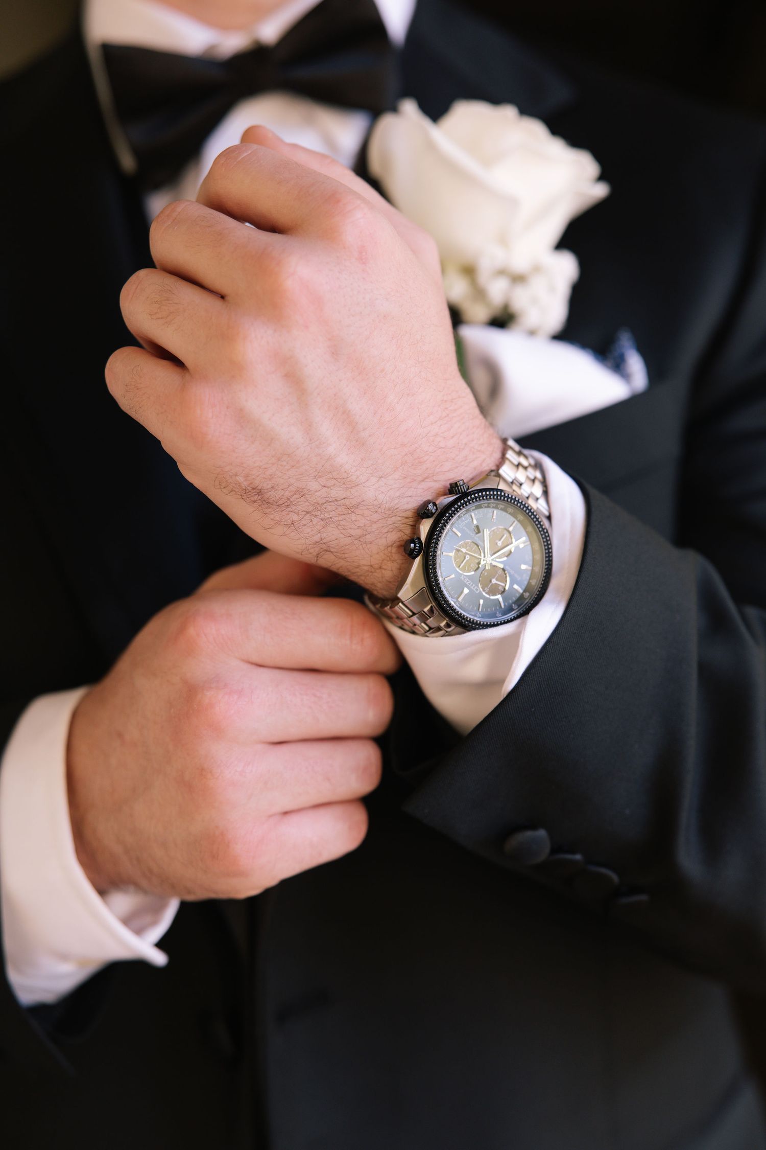 Close-up shots of hands adjusting a silver wristwatch against a black suit.