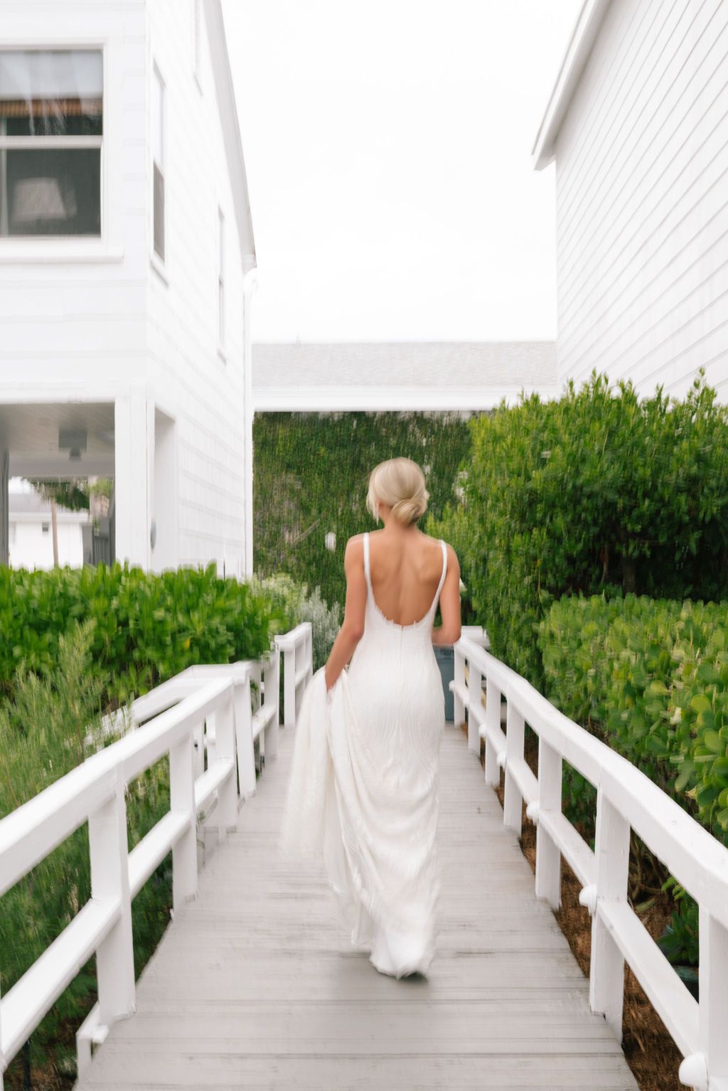 Bride walking away on white wooden boardwalk surrounded by lush greenery.