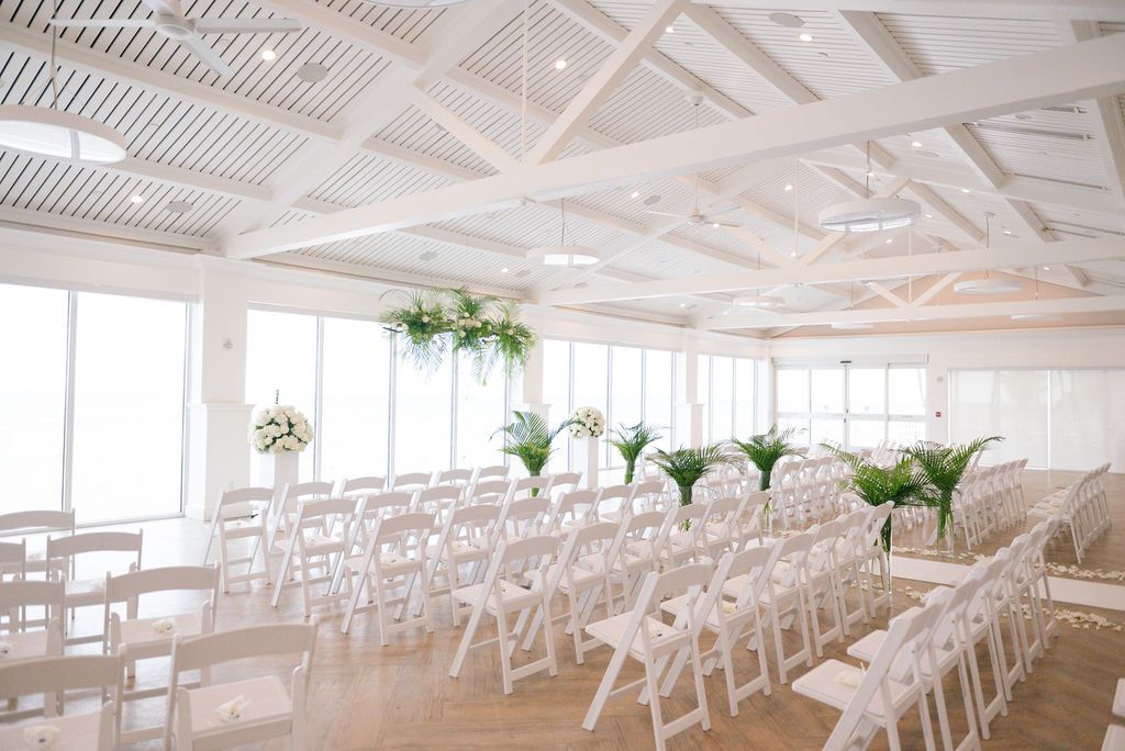 Bright minimalist wedding venue with white chairs and scattered rose petals creating an aisle.