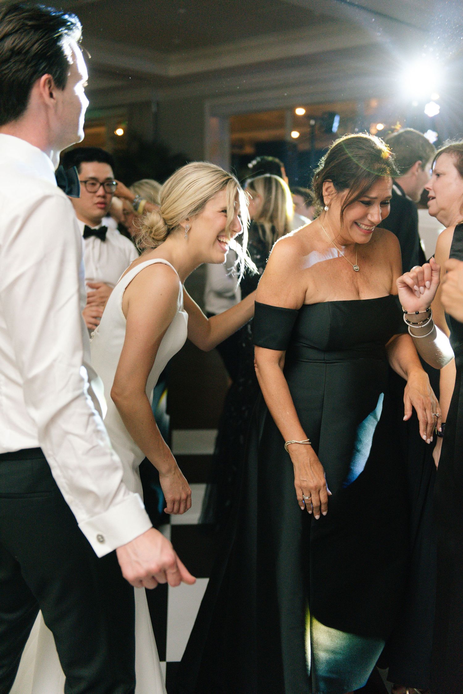 Wedding guests dancing and laughing together at a reception with elegant black and white formal attire.