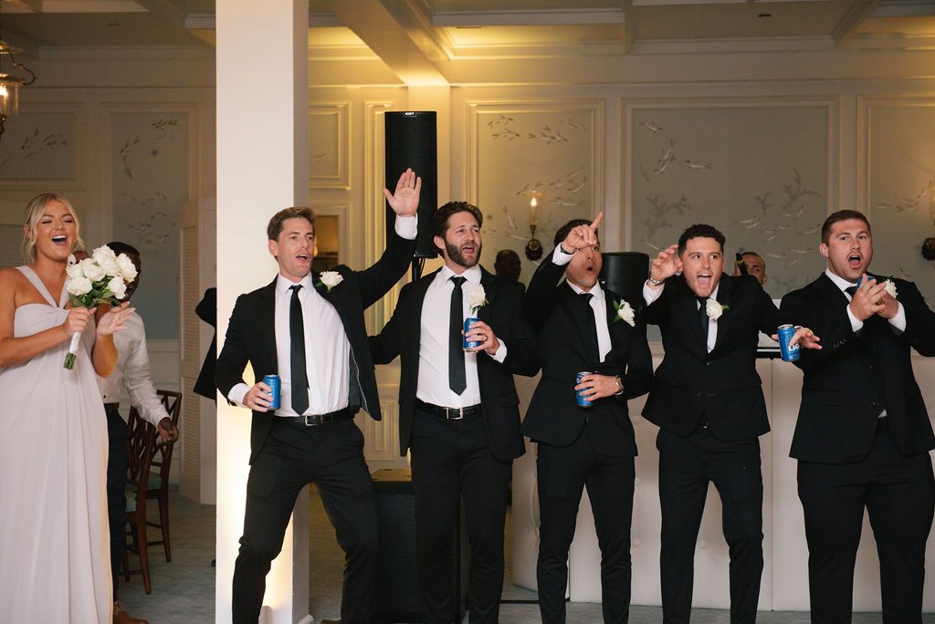 Wedding party in formal black and white attire lined up in an elegant ballroom.