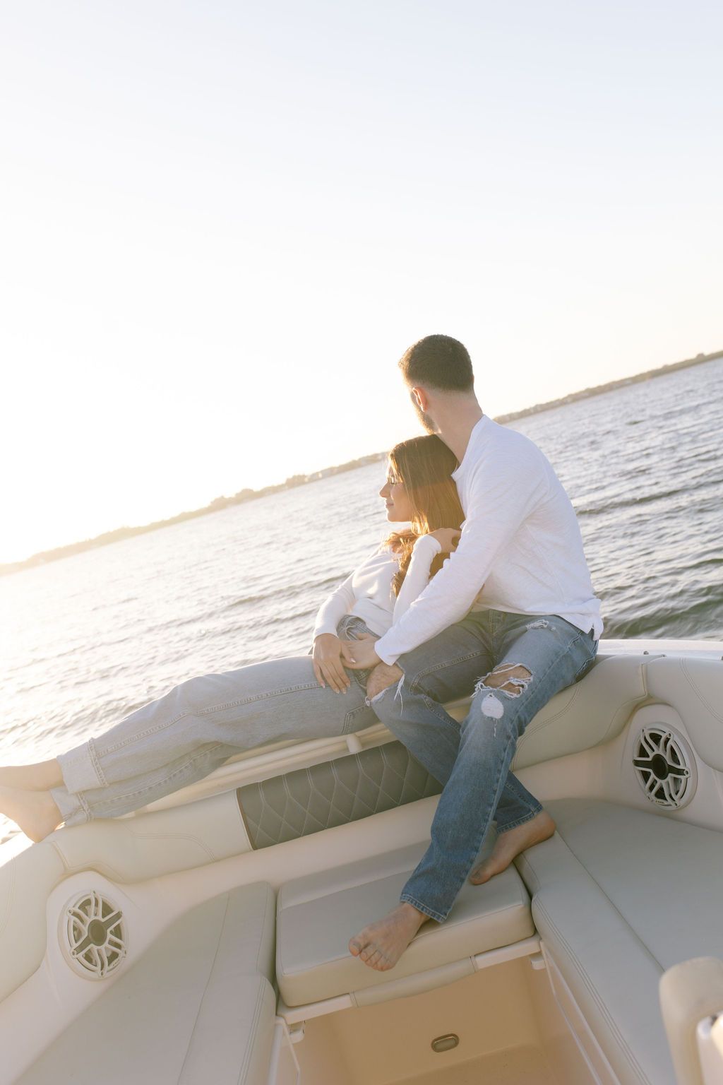 Couple sitting close together on boat edge overlooking calm waters at sunset.
