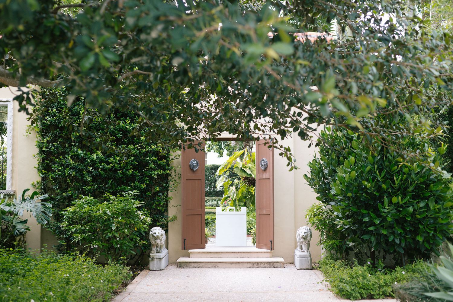Garden archway with lush greenery leading to a pink stucco entrance.