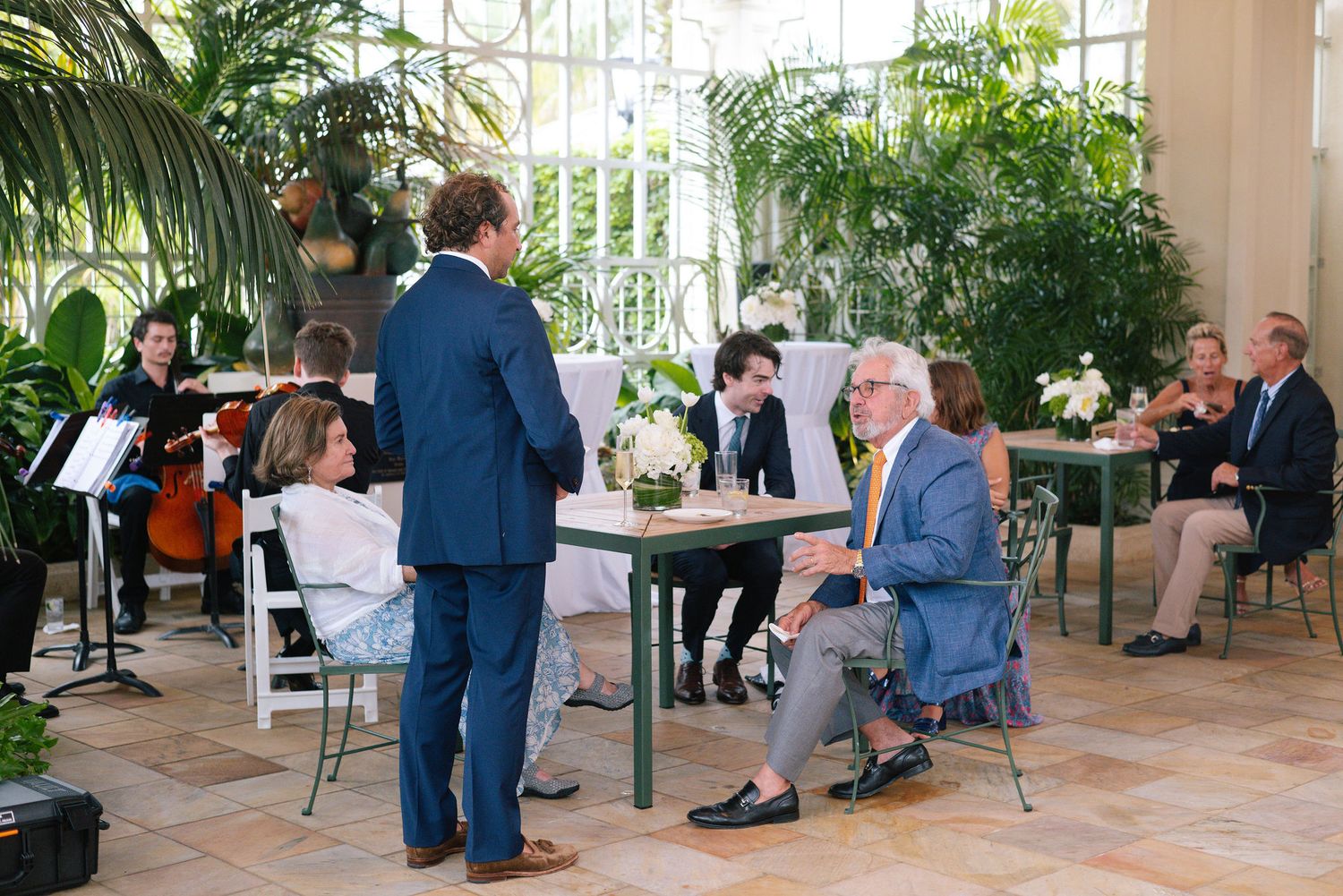 Indoor garden reception space with guests seated among lush tropical greenery.