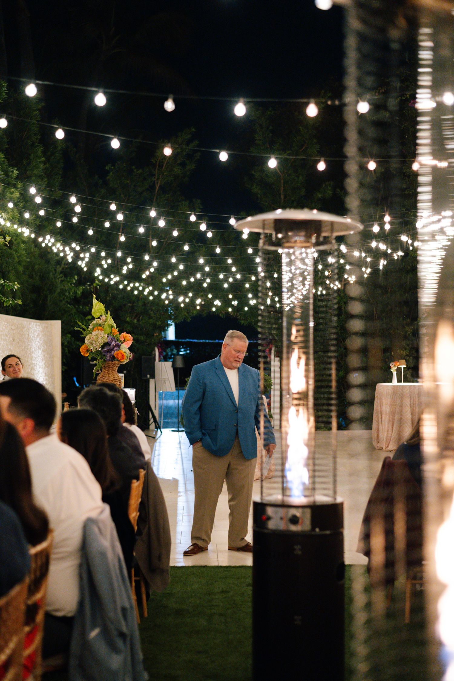 String lights illuminate an outdoor evening reception space with palm trees.