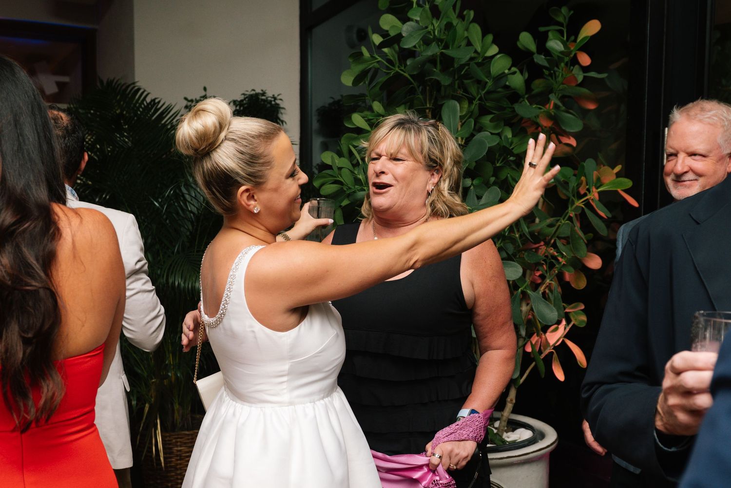 People dancing and celebrating at a lively party with indoor plants in the background.