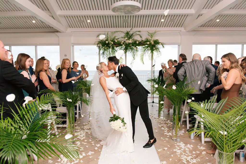 Wedding party dancing and celebrating at a white-themed reception with tropical palm decor.