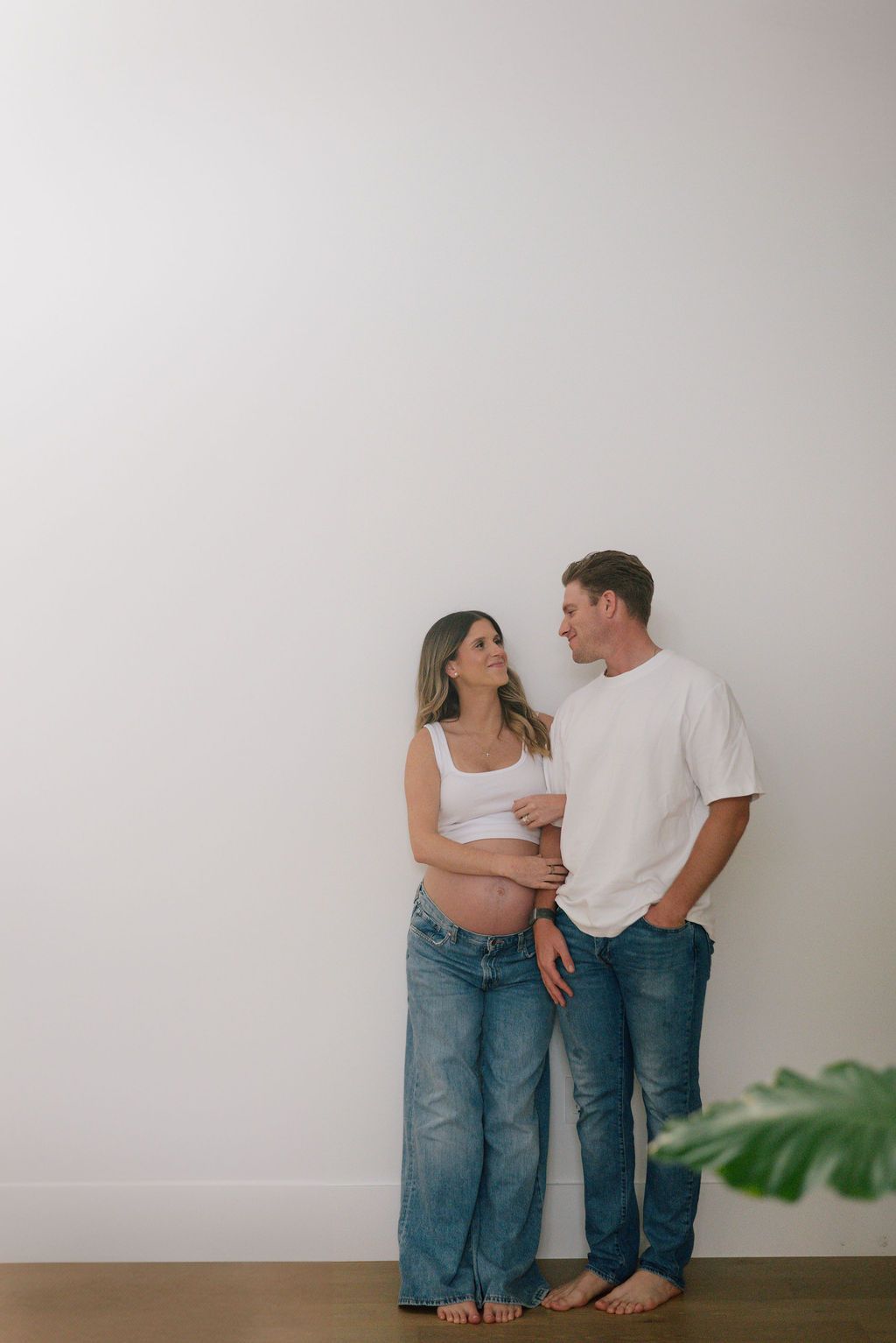 A couple in matching denim stands together against a white wall for a casual photoshoot.