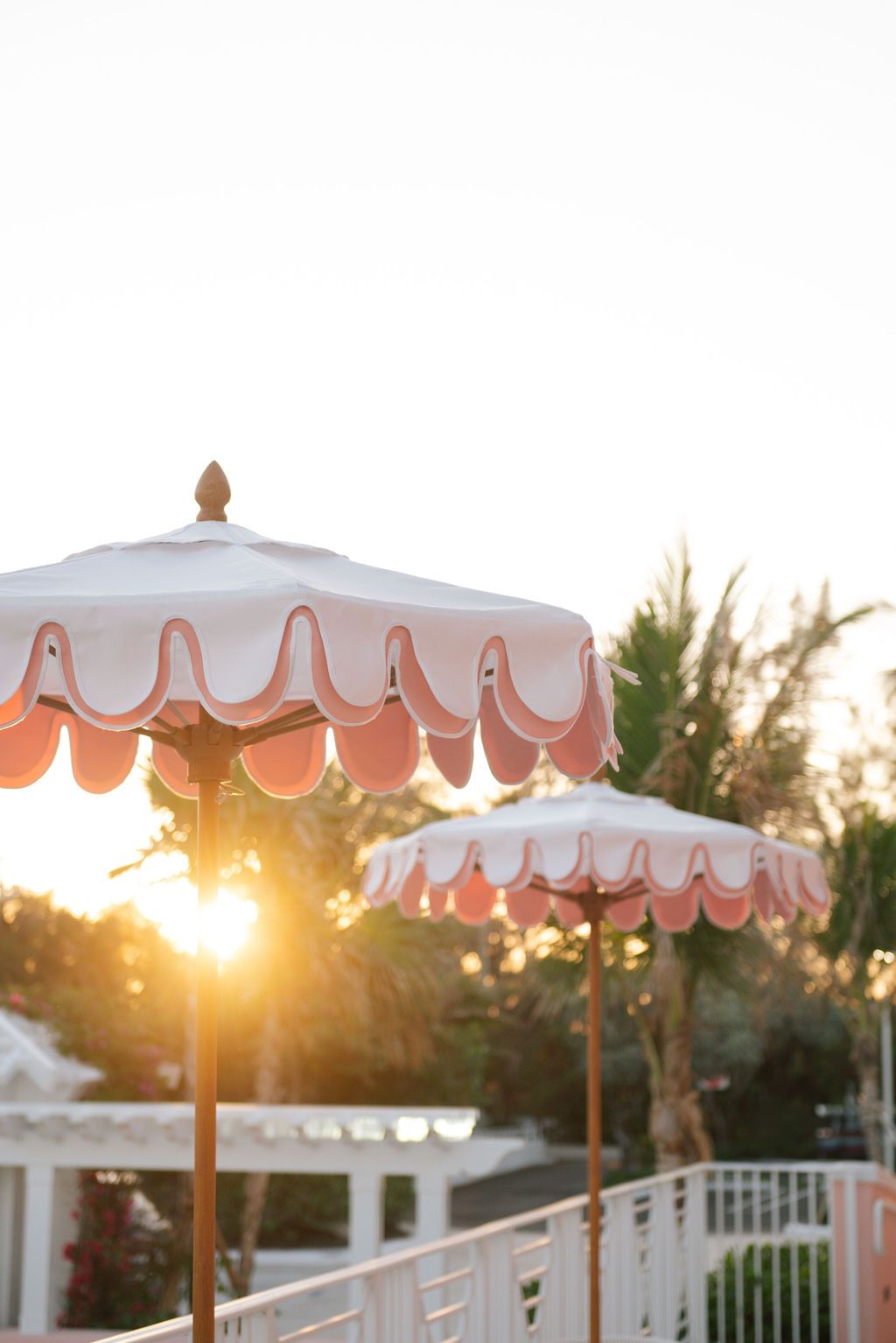 Scalloped coral and white umbrellas backlit by golden sunset light on a resort patio.
