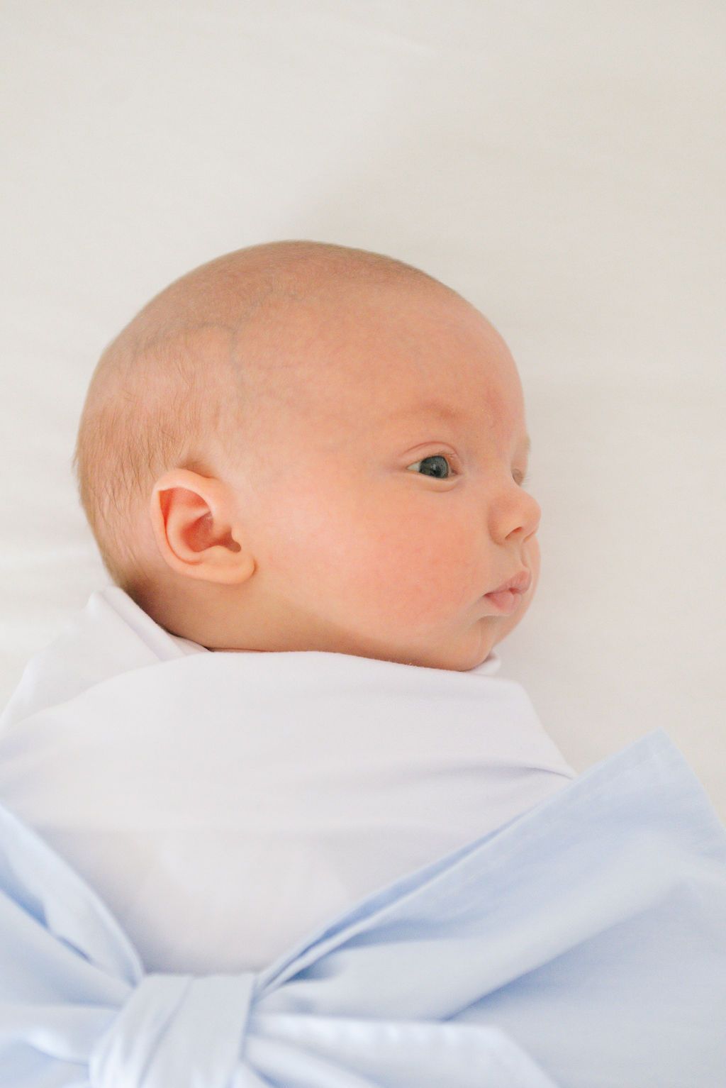 Side profile of a newborn baby wearing white with a light blue bow accent.