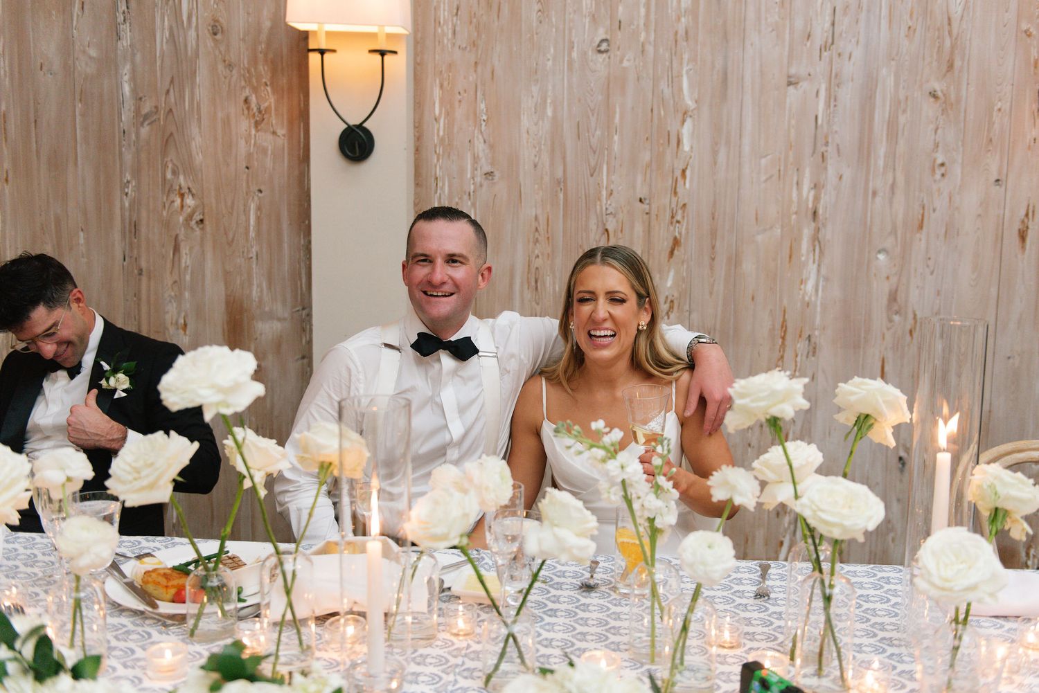 Couple sitting at decorated wedding reception table with white floral arrangements.