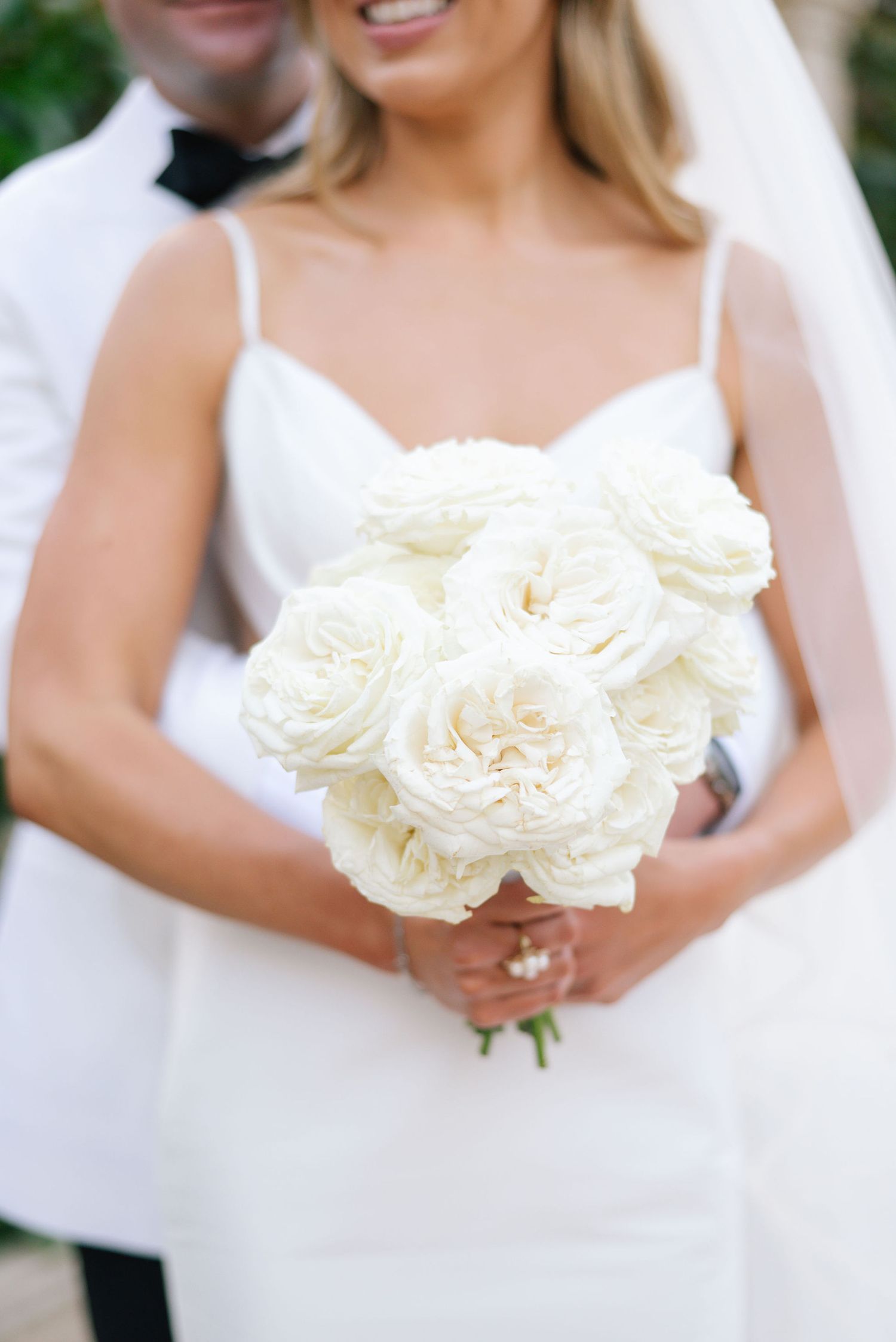 Close-up of elegant white roses in a bridal bouquet against a light background.