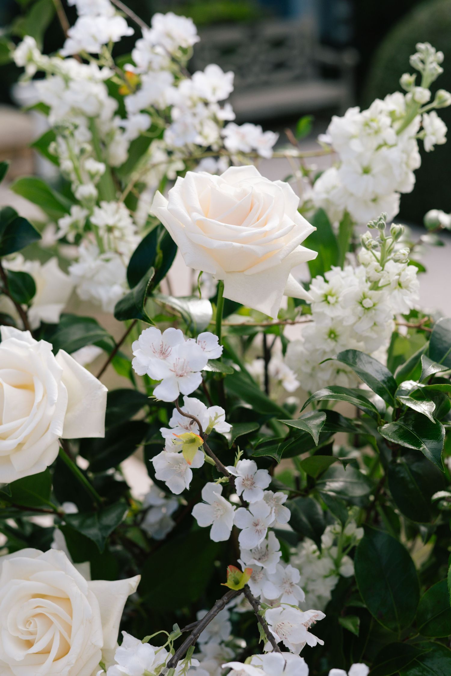 Delicate white roses and small floral blooms arranged with lush green foliage create a romantic wedding display.