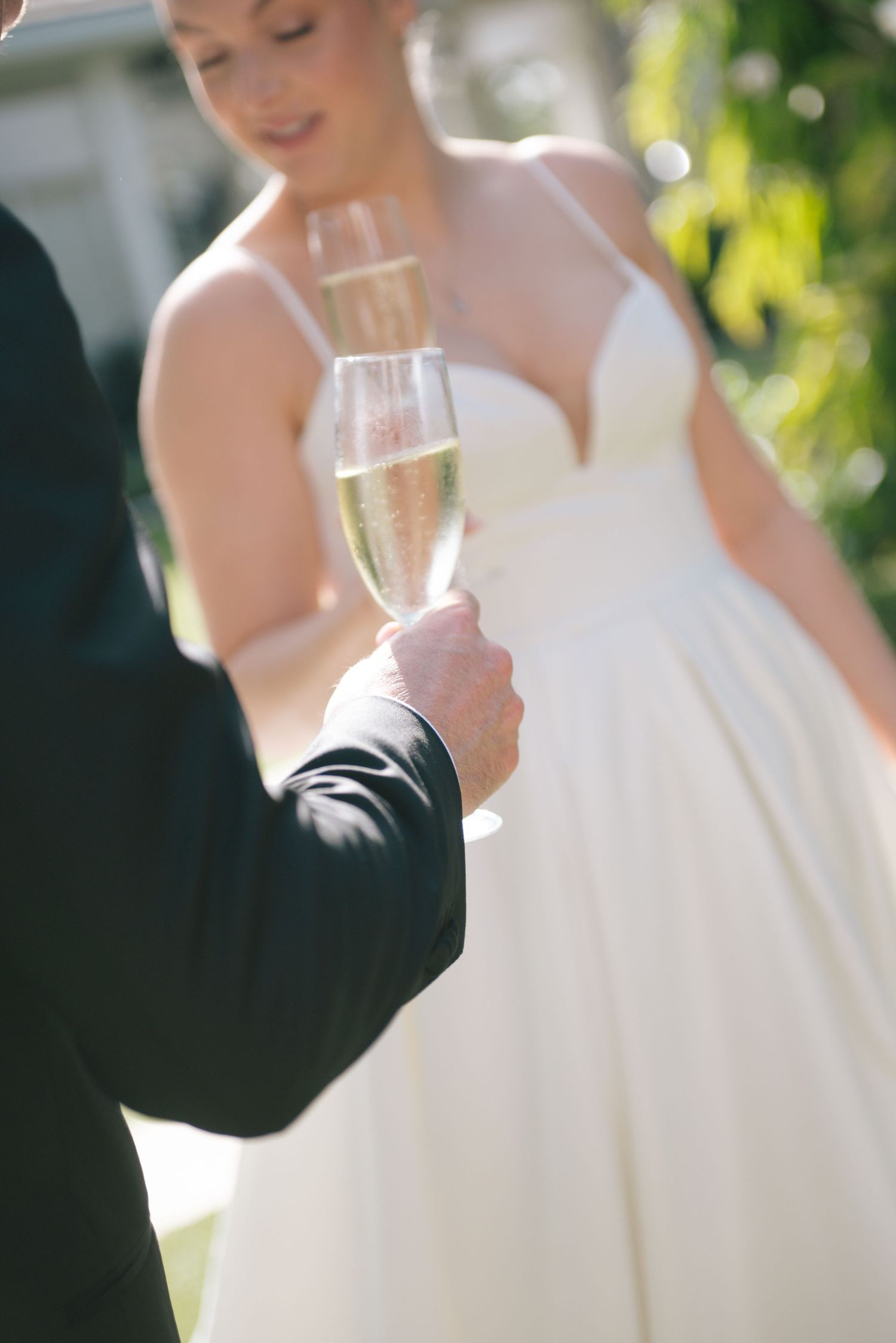 Wedding toast moment in sunlit garden with champagne glasses and white dress.