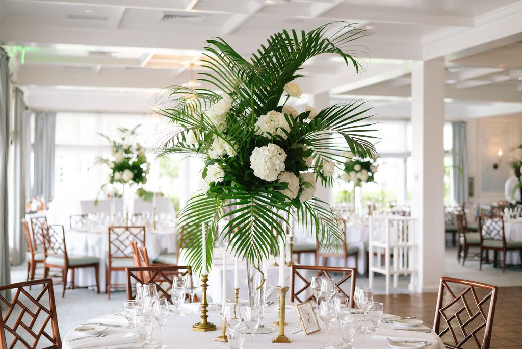 Bright banquet hall with white tablecloths, tropical centerpieces and wooden chairs.