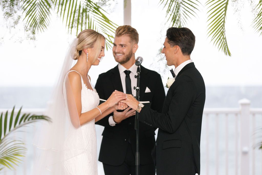 Wedding ceremony exchange of rings under tropical palm leaf decorations.
