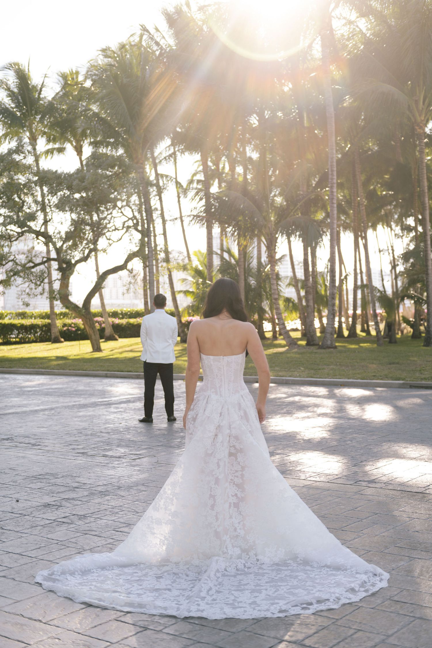 Wedding dress silhouette against palm trees and sunset light on stone patio.