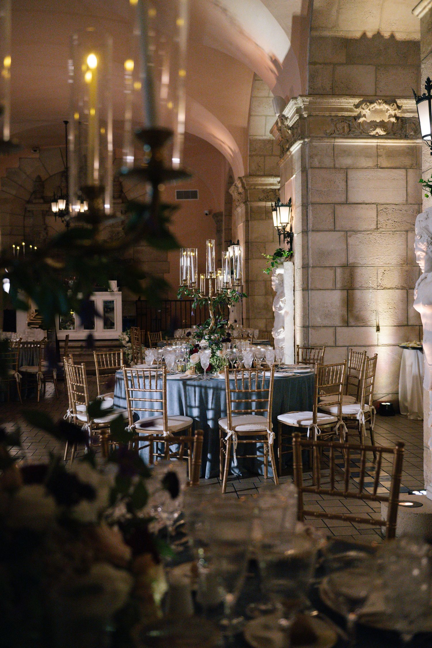 Stone pillared reception hall with elegant table settings and ambient lighting creating a romantic atmosphere.