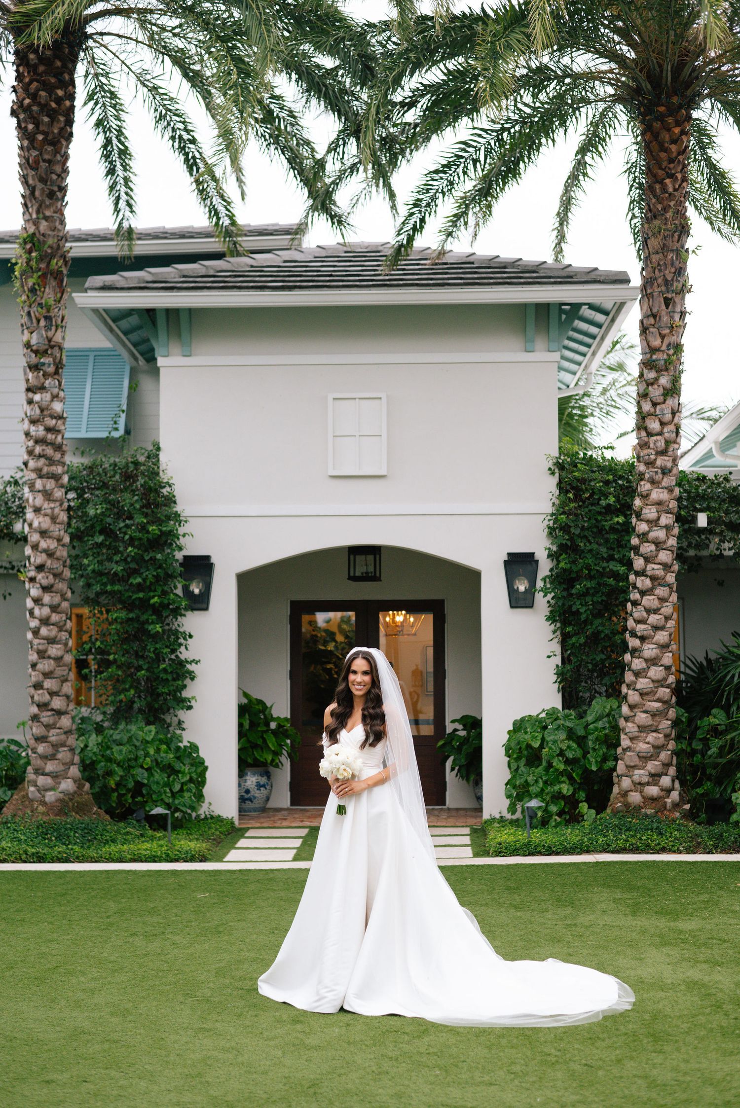 Elegant white wedding dress with long train photographed on manicured lawn with palm trees.