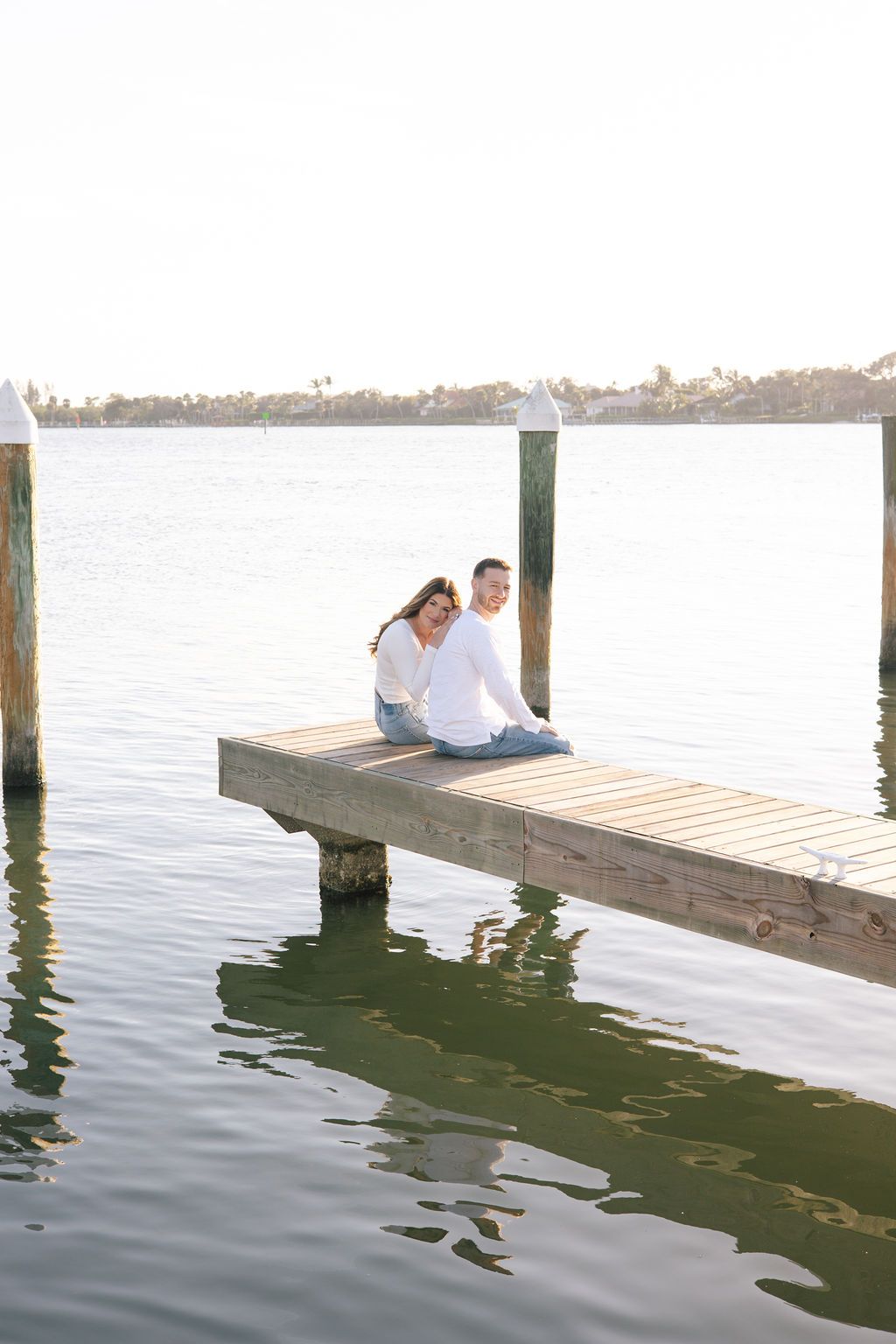 Couple sitting together on wooden pier over tranquil water.