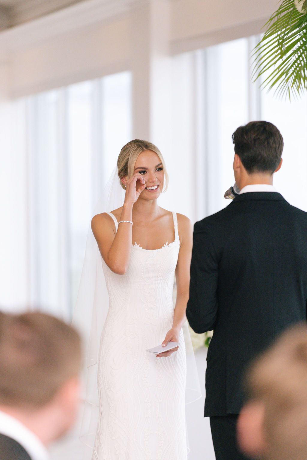 Emotional moment during wedding ceremony in bright white venue with palm decor.