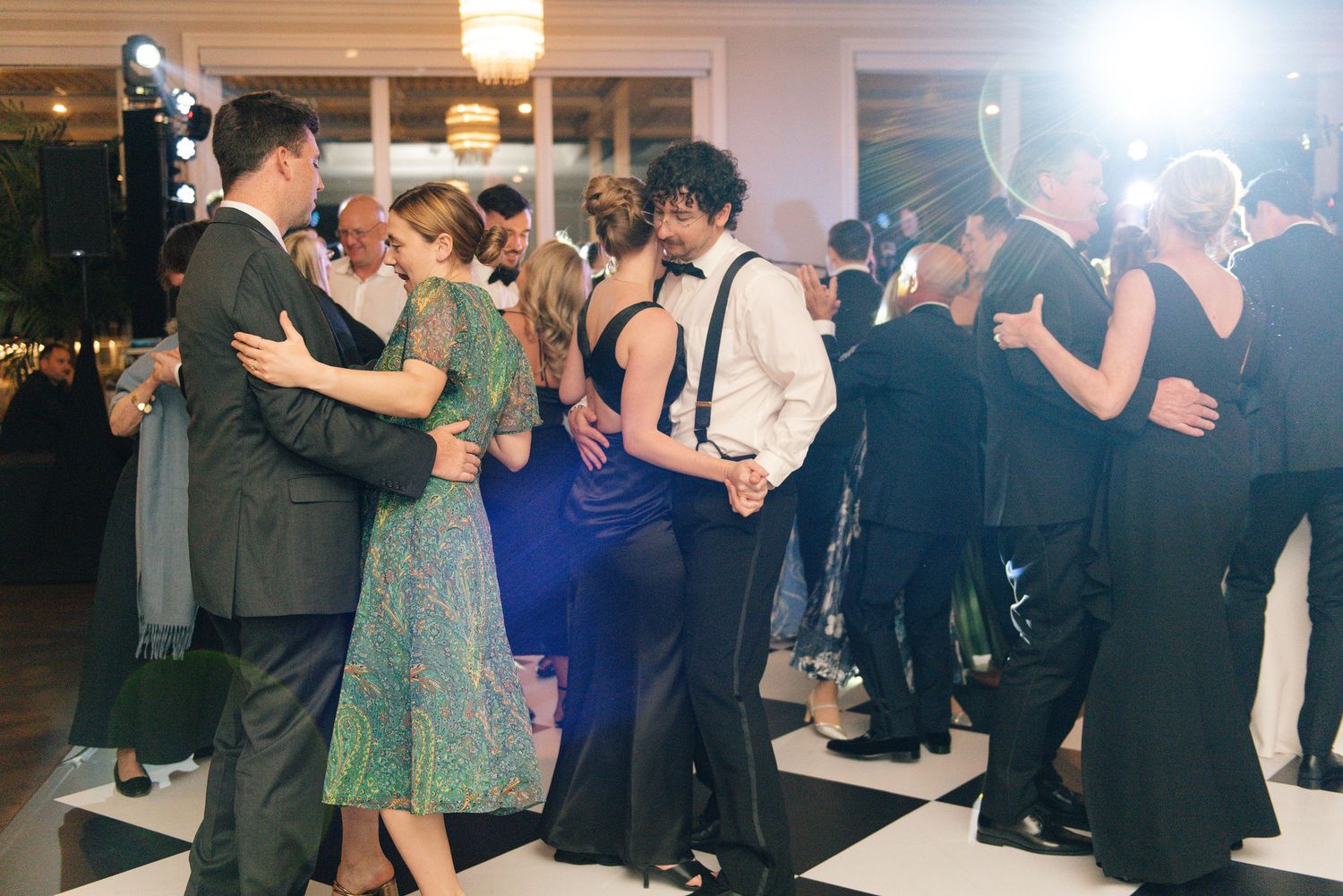 Wedding guests dancing together at an evening reception with dramatic lighting.