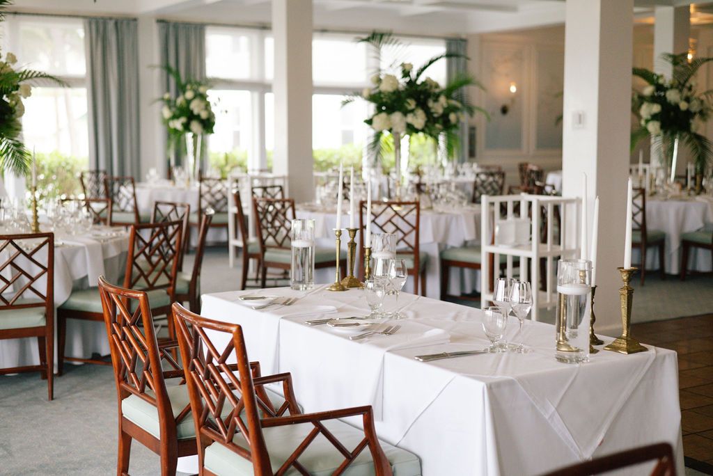 Elegant white dining room with wooden chairs and table settings for a formal event.