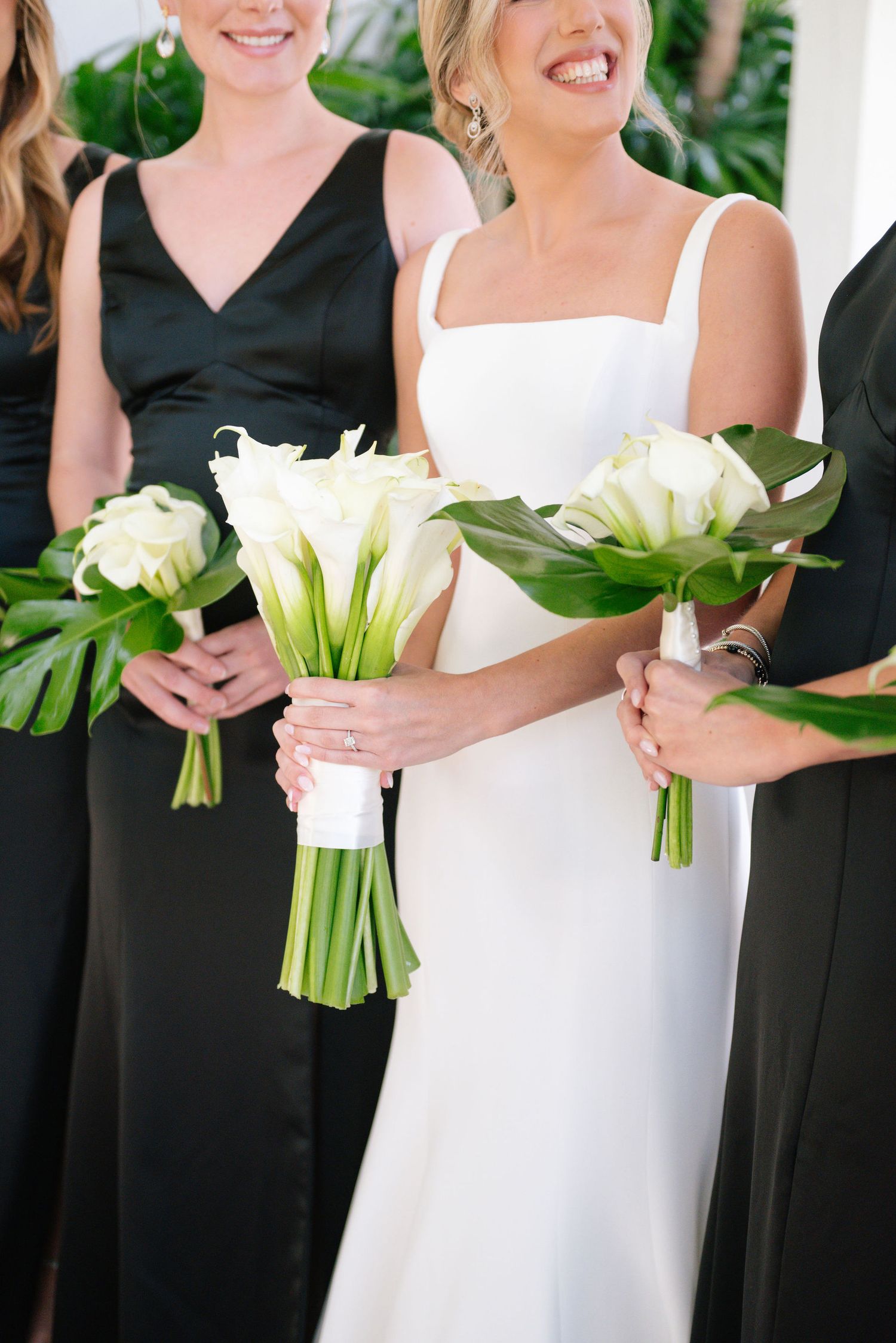 Wedding party holding elegant white calla lily bouquets against black dresses.