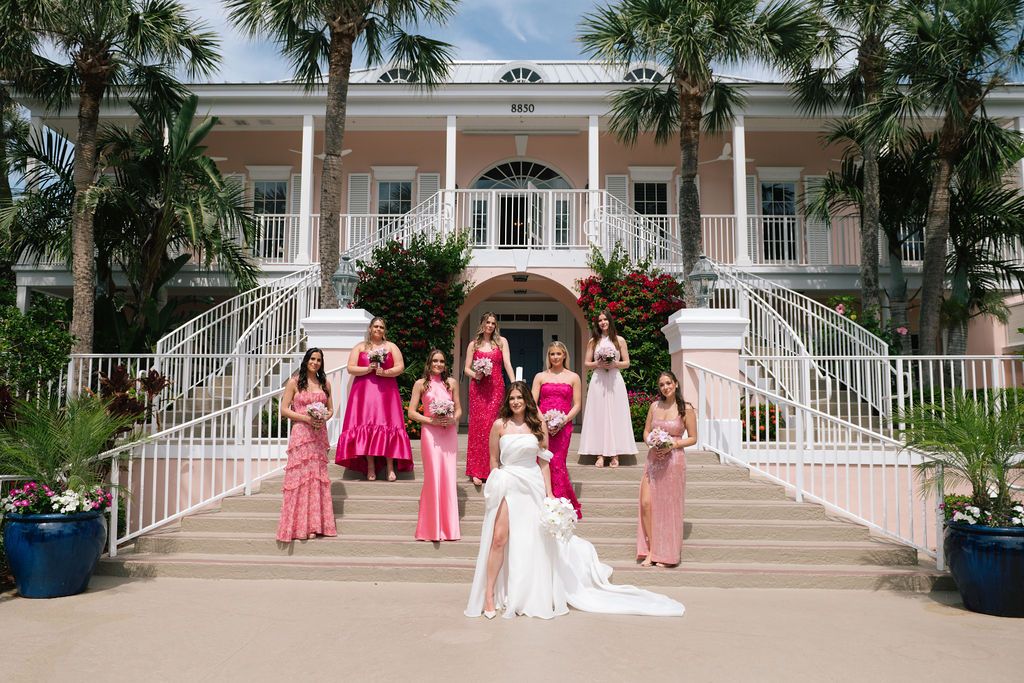 Wedding party poses on grand white stairs of a southern mansion with palm trees.