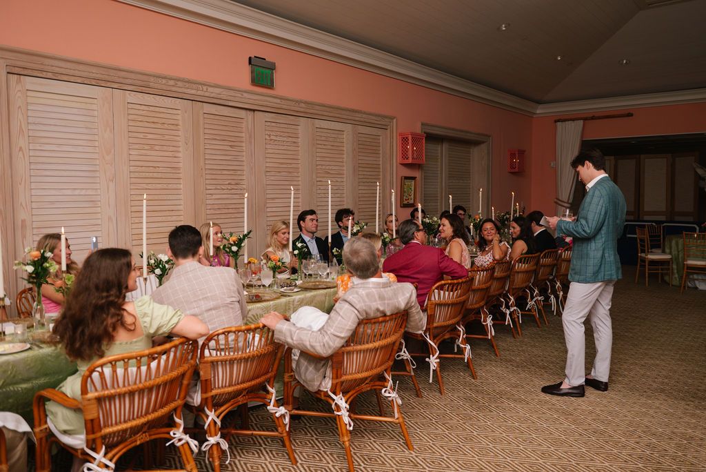 Formal dinner gathering with guests seated at long tables in a coral-colored dining room.