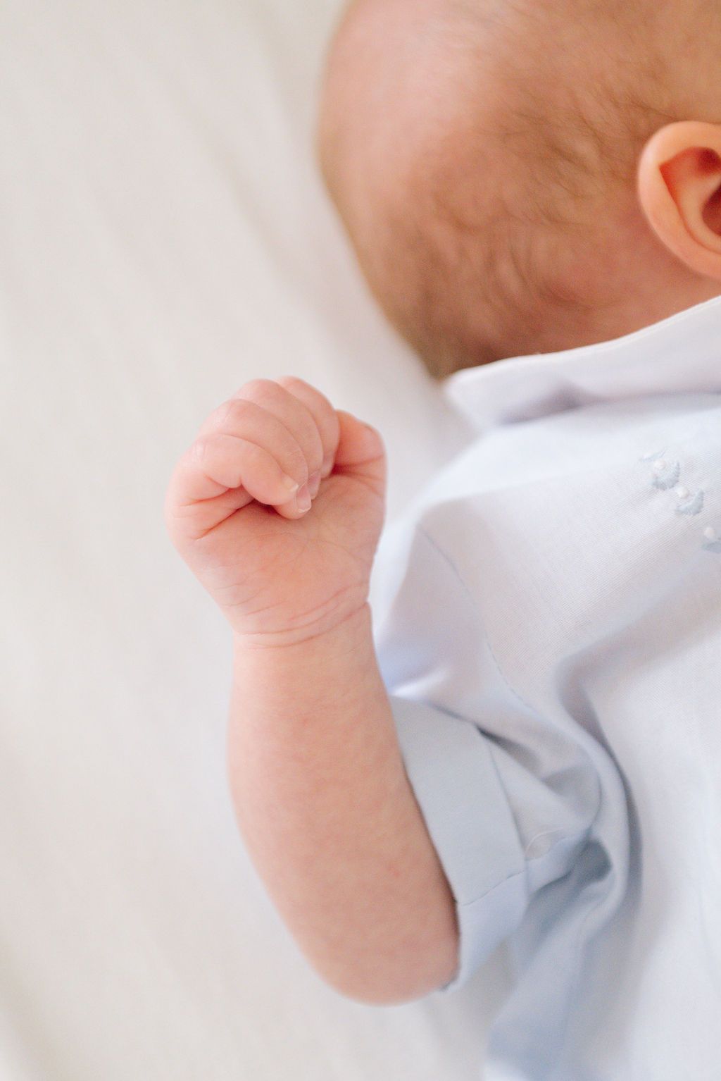 Close-up of a baby's small hand and arm wearing a white onesie.