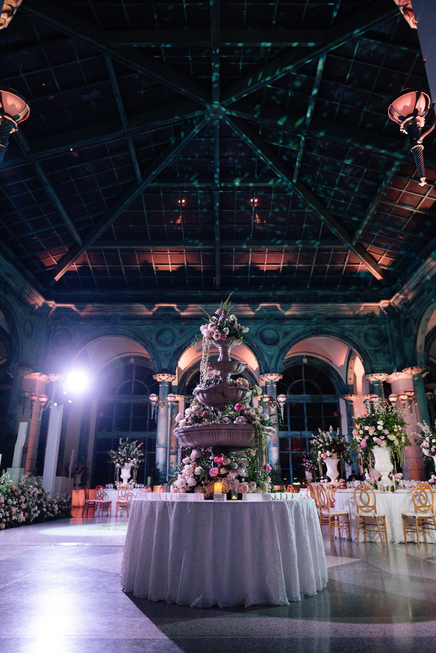 Grand ballroom set for an elegant reception with round tables and dramatic overhead lighting.