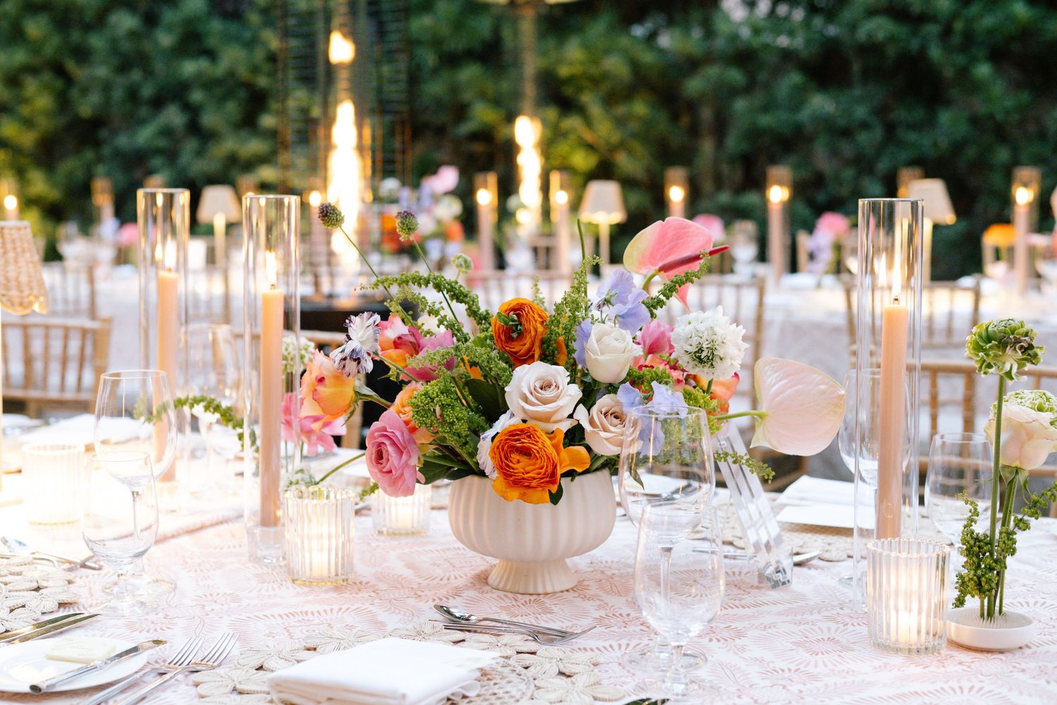 Romantic table setting with colorful floral centerpiece and glass candleholders at outdoor reception.
