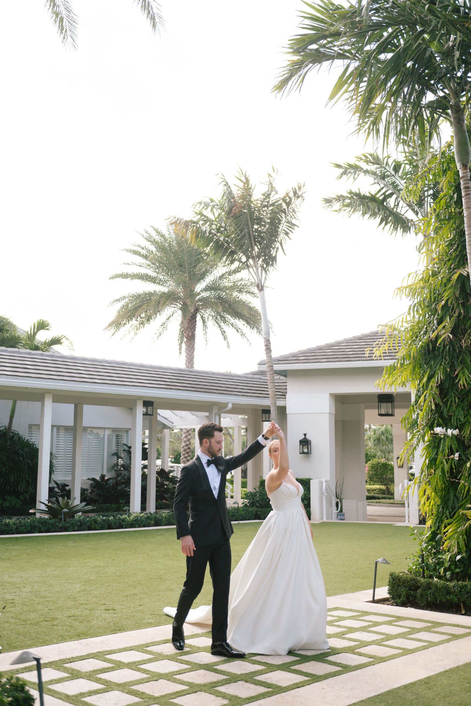 Wedding couple dances and twirls on a garden path surrounded by palm trees.