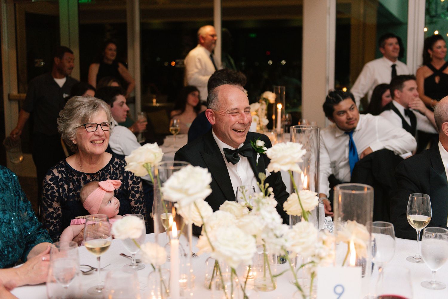 Wedding reception dinner table decorated with white floral centerpieces and candlelight.