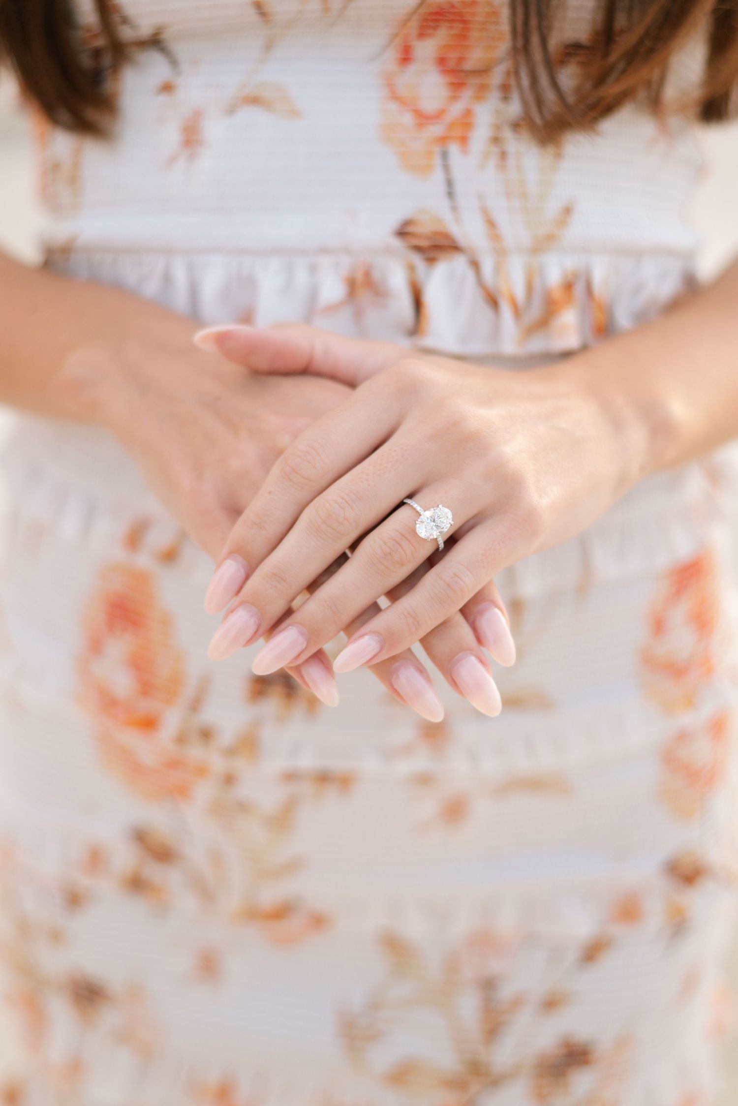 Close-up of engagement ring on hand with floral dress in background.