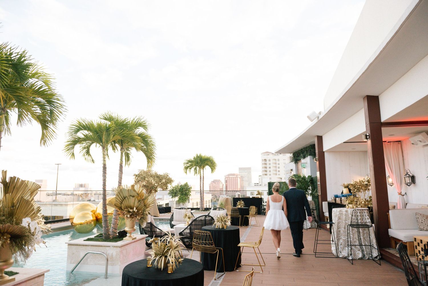 Panoramic view of a beachfront venue with white chairs and palm trees against a cloudy sky.