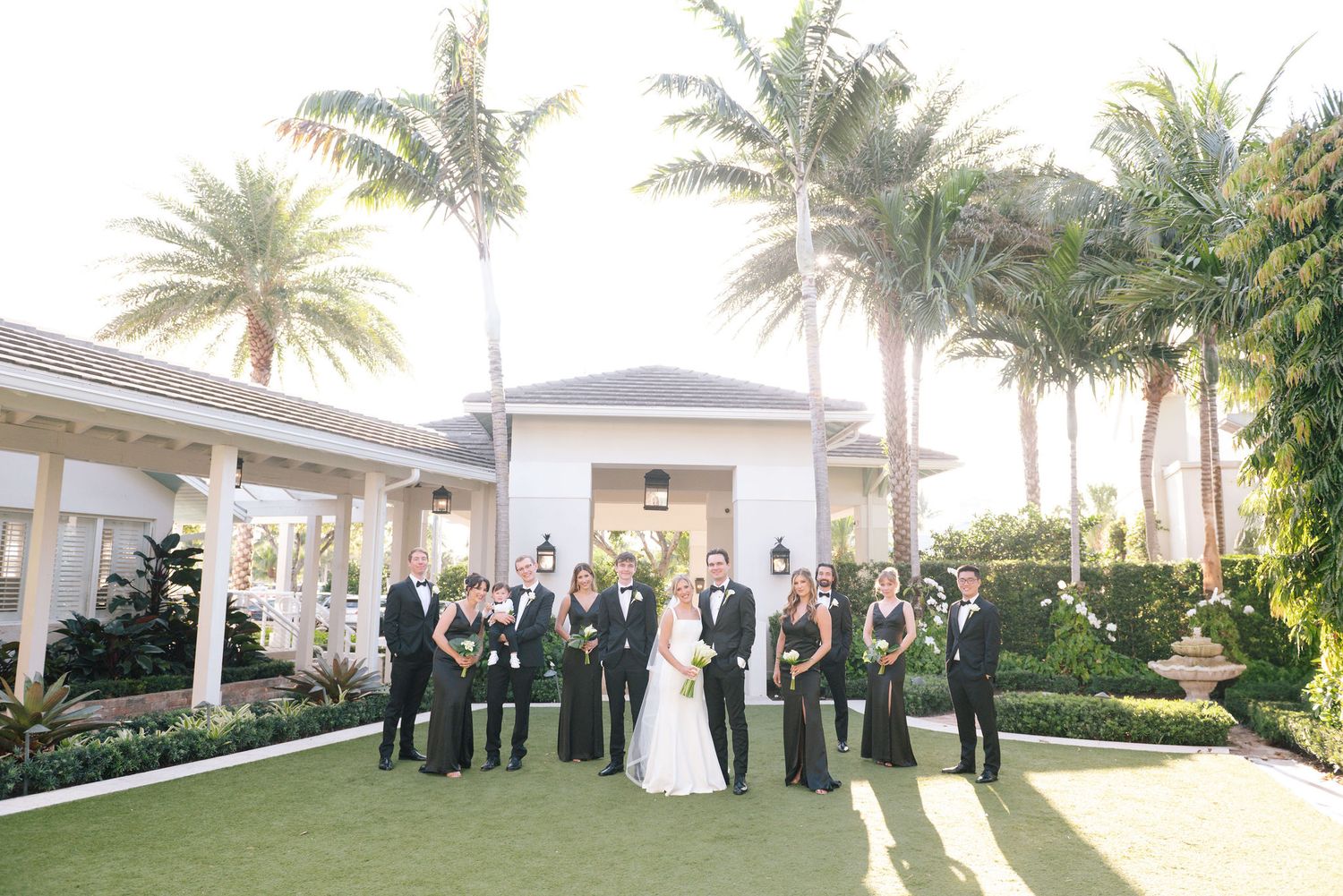 Wedding party walking along a palm tree-lined path at an elegant venue.