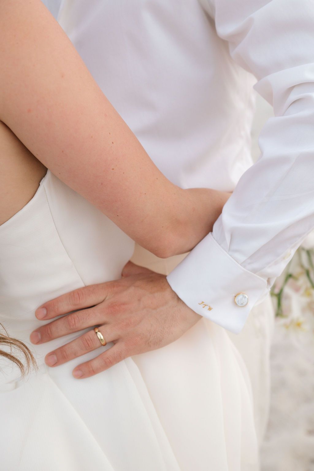 Close-up details of wedding rings and hands against white formal attire.